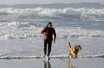 PACIFIC GROVE, CA - FEBRUARY 07: A woman runs with her dog along the beach February 7, 2006 in Pacific Grove, California. The U.S. saw its warmest January on record with a national average of 39.5 degrees Fahrenheit, beating the old record for January temperatures of 37.3 degrees set in 1953. Due to the unseasonably warm weather, Americans have been able to save on heating bills just as oil prices have hit record highs. Temperatures in the Monterey Bay are expected to in the 70's with clear skies for the next five days. (Photo by Justin Sullivan/Getty Images)