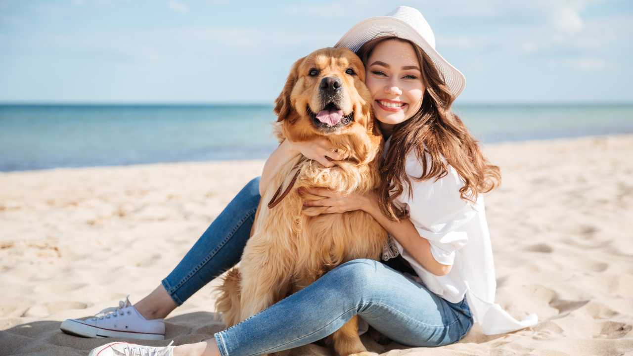 ragazza che abbraccia il proprio cane sulla spiaggia Cane in spiaggia, cosa stabilisce la legge